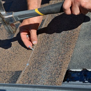 Contractor installing bitumen roof shingles with hammer and nails. Contractor installing bitumen roof shingles with hammer and nails.